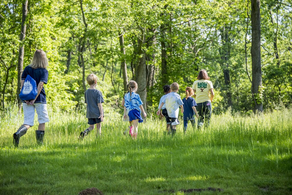 group of four children and two adults walking in grass field