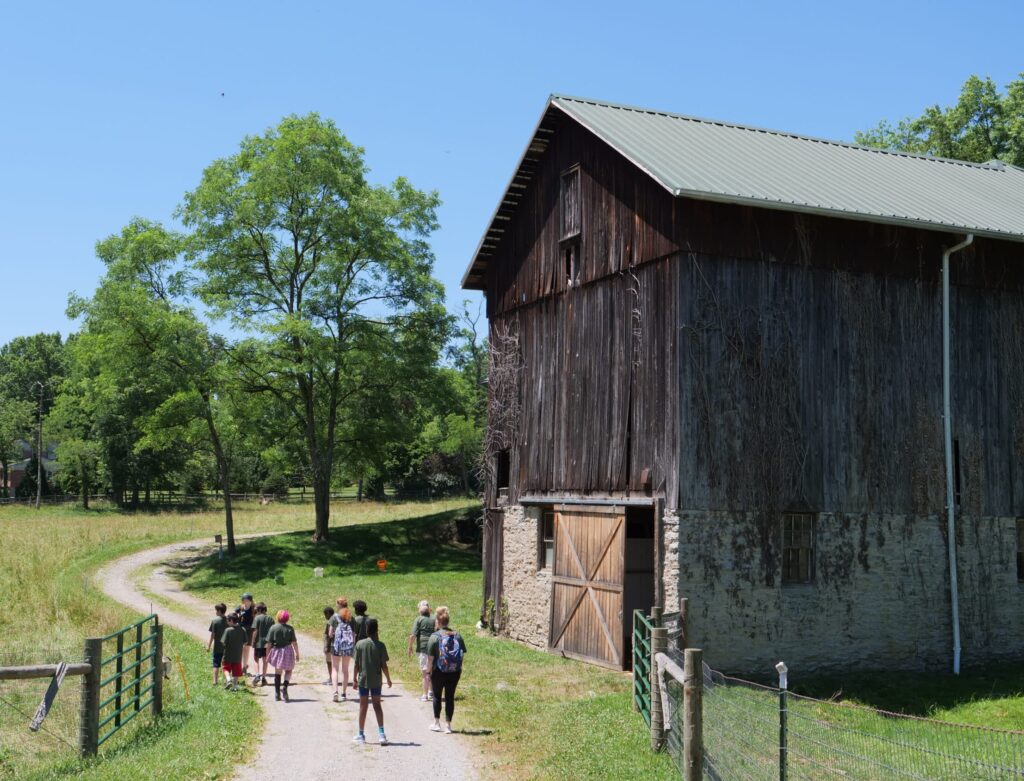 educators leading children on gravel path near old wooden barn and pasture