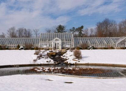 Snow-covered large Greenhouse with pond in front.