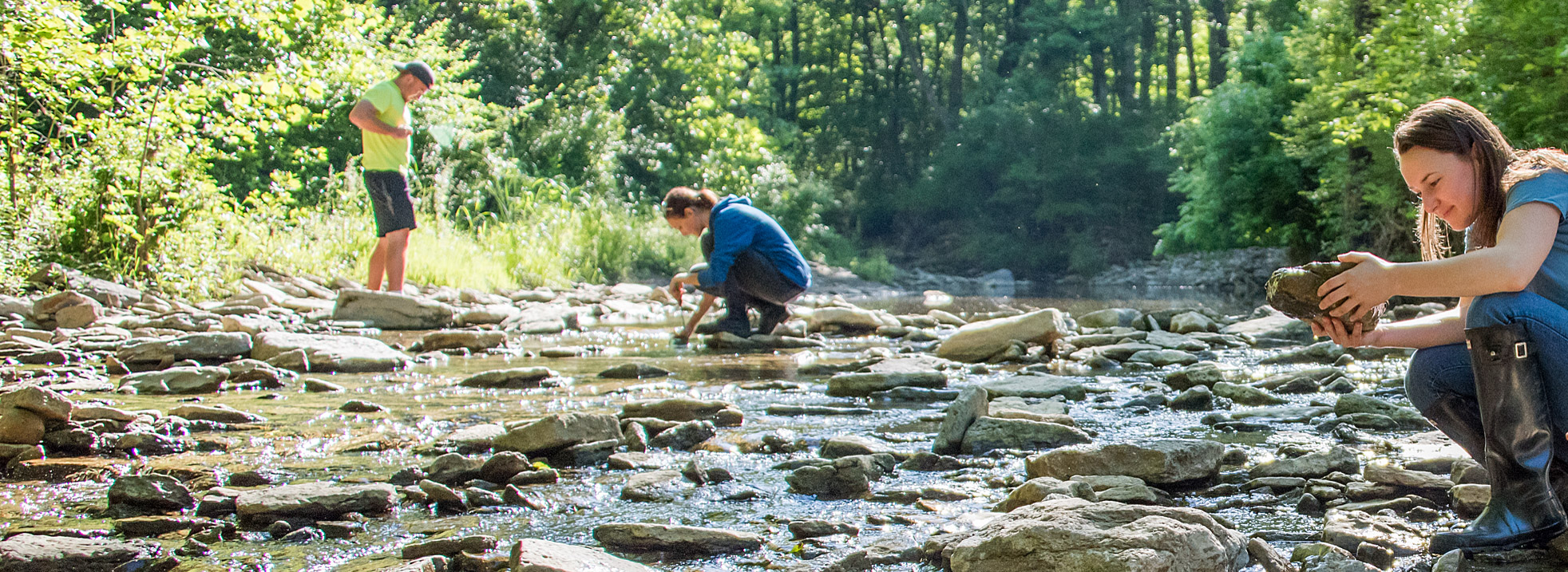 Three educators exploring creek and observing rocks